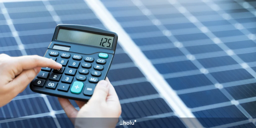 Mão de uma pessoa segurando uma calculadora em frente a placas solares