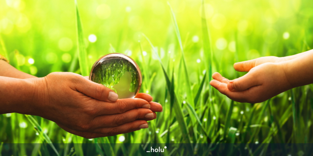 Foco nas mão de uma pessoa passando um olha grande de agua, que reflete o gramado atrás, para a mão de uma criança